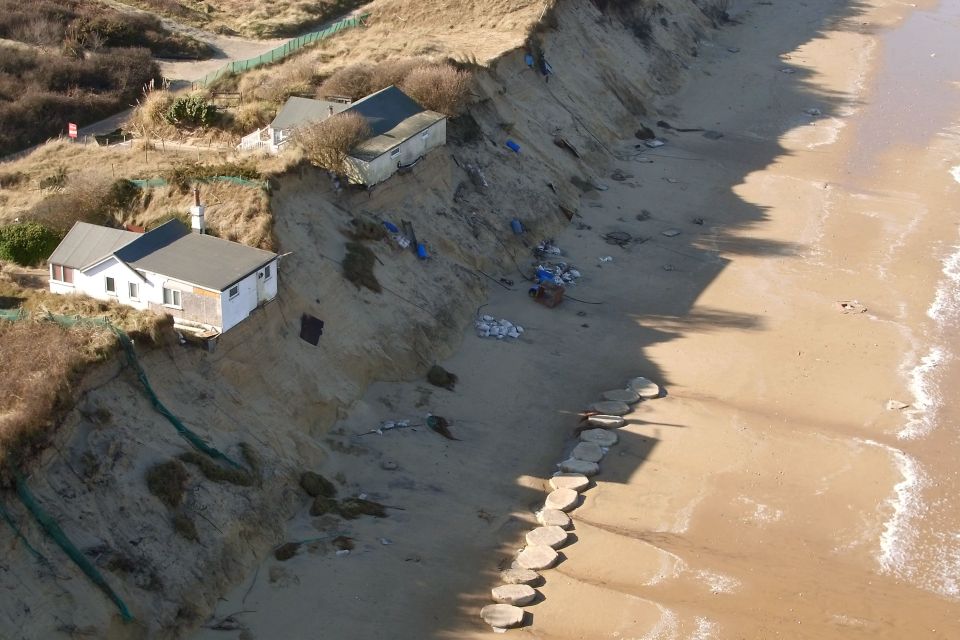 Houses on a severely eroded cliff edge above the sea.