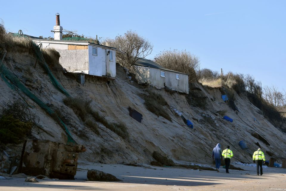 Emergency services personnel walk past houses on a cliff edge eroded by bad weather.