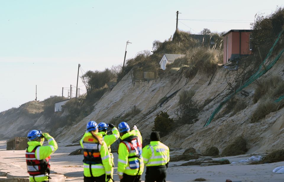 Emergency services personnel looking at houses on an eroded cliff edge.