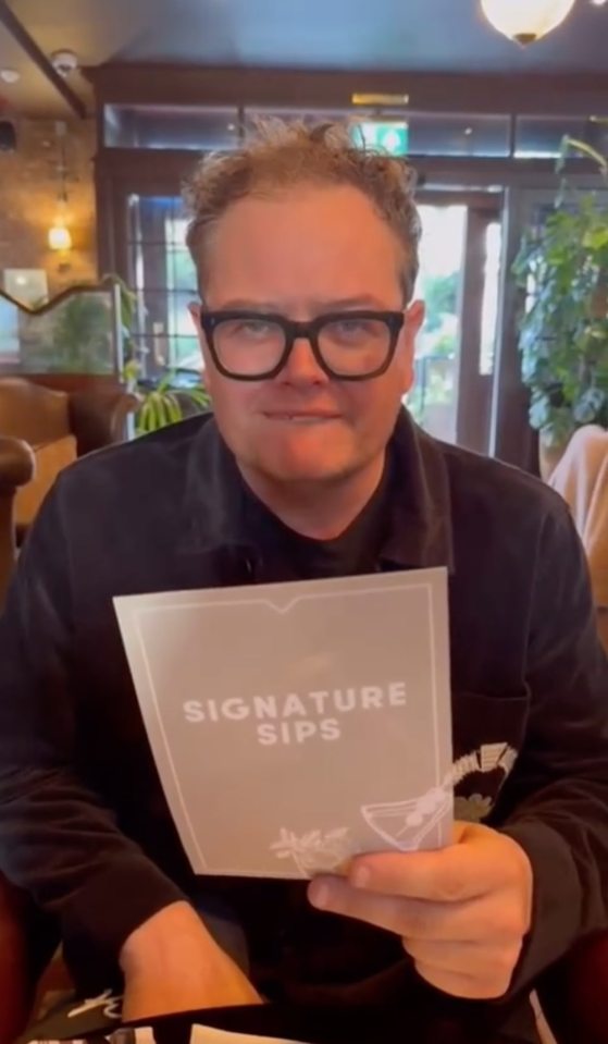 Alan Carr holding a menu that reads "Signature Sips".