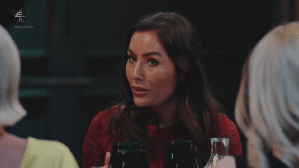 A woman with dark hair and a red top speaks at a table.