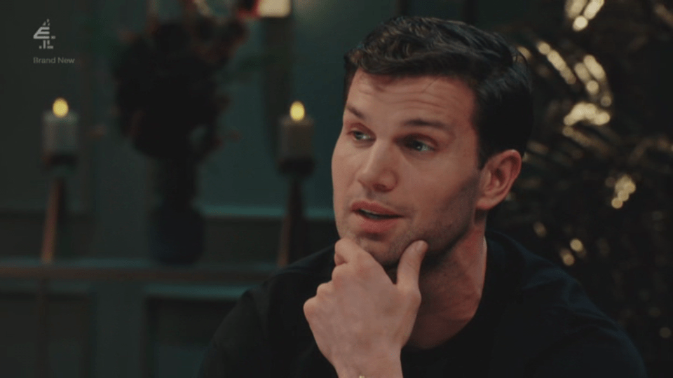 A man with dark hair holding his chin, looking contemplative.