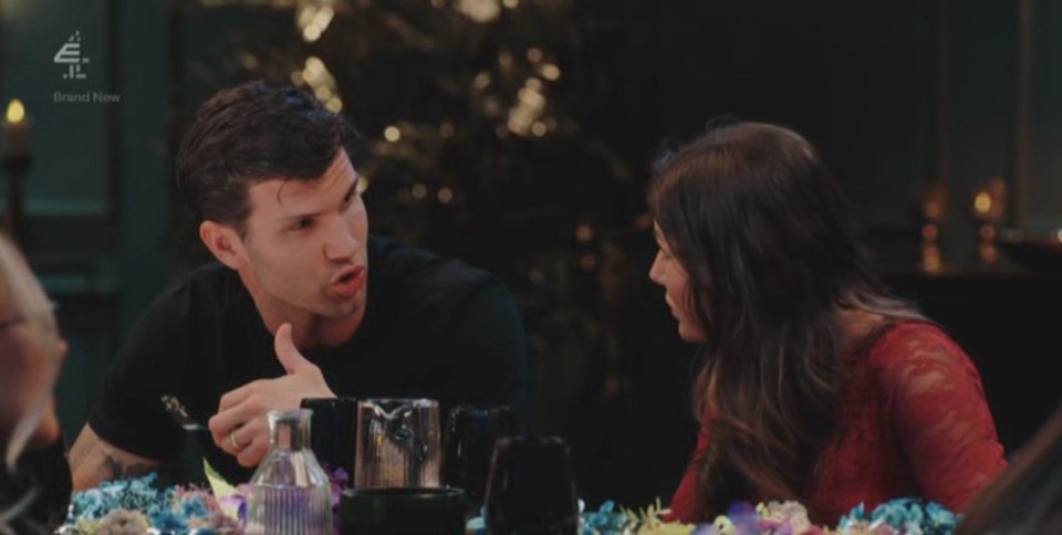 A man in a black shirt gestures while speaking to a woman in a red lace top across a flower-decorated table, with the subtitle "To me that's immature."