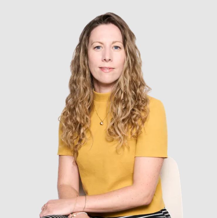Doctor Danielle Brightman, a woman with long, curly blonde hair, wearing a yellow top and striped trousers.