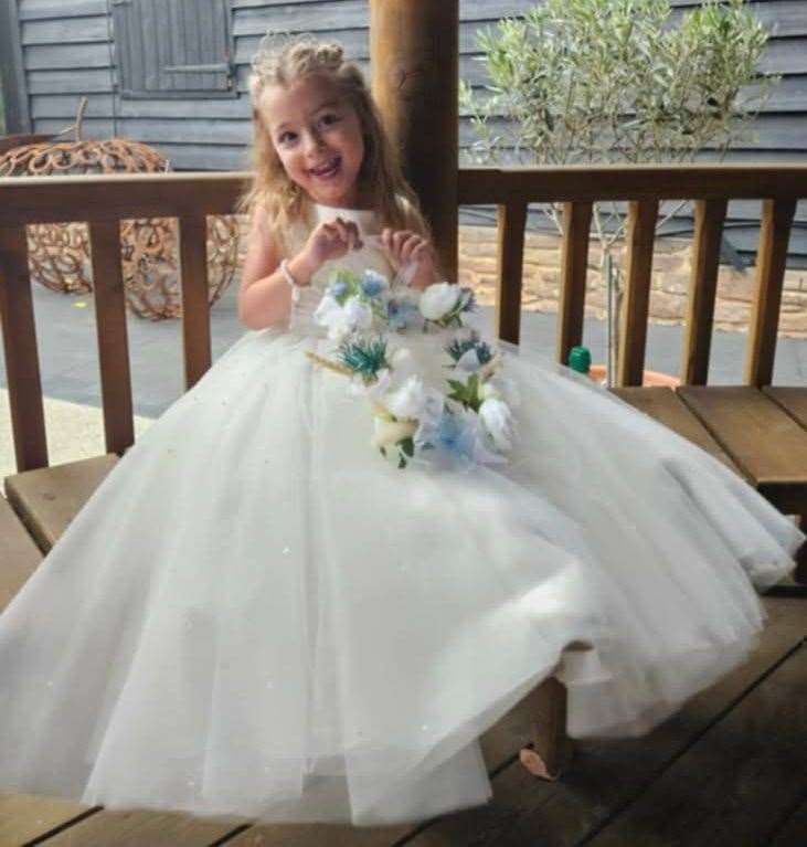 Luna Ivy Webster smiling while wearing a white dress and holding a bouquet of flowers.