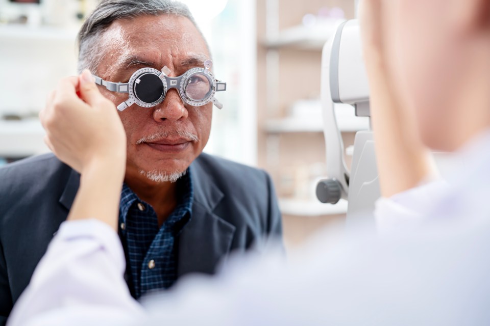 An older man having his eyes examined by an optometrist using a phoropter.
