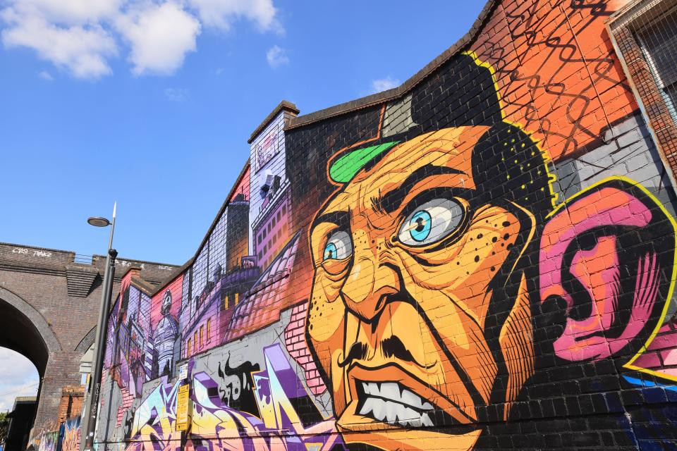 Street art featuring a colorful, aggressive-looking face with blue eyes and brick archways in Digbeth.