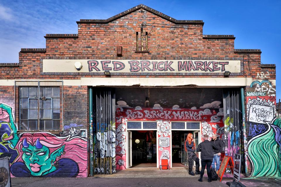 Red Brick Market in Digbeth, Birmingham, with vibrant graffiti, open doors revealing merchandise, and a few people gathered outside.