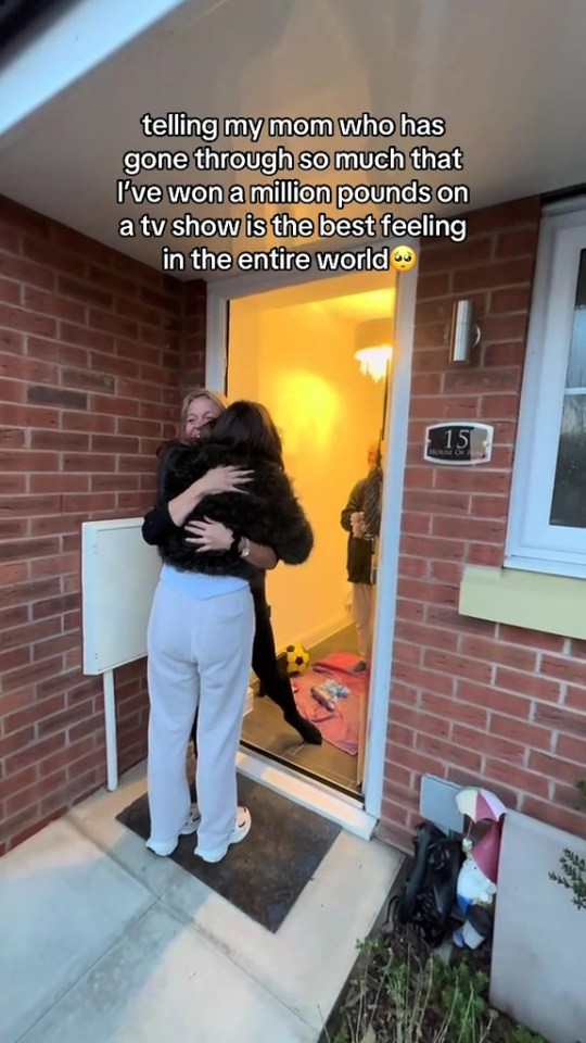 A woman in white pants and black jacket embracing her mom in the doorway of a brick house.