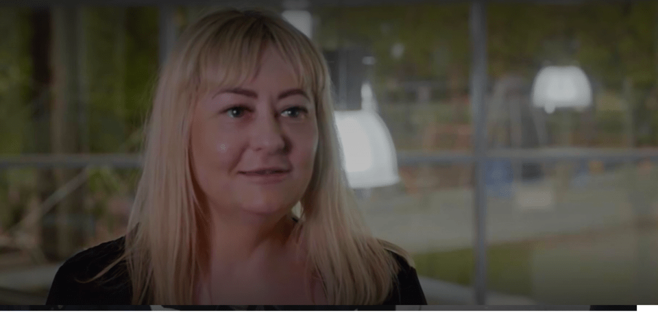 A woman with blonde hair and bangs, smiling subtly.