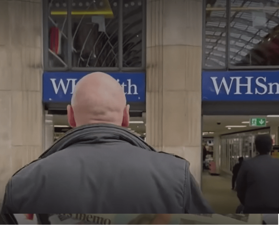 Rear view of a bald man with a black jacket following another person into a WHSmith store.