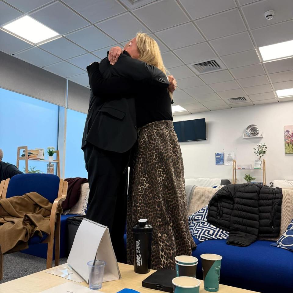 Two people hugging in an office or lounge area.