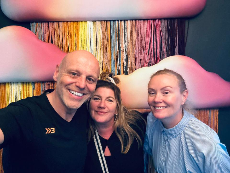 Speaker presenting on stage to an audience in a darkened room, with a screen displaying "PROGRAM YOURSELF FOR SUCCESS"