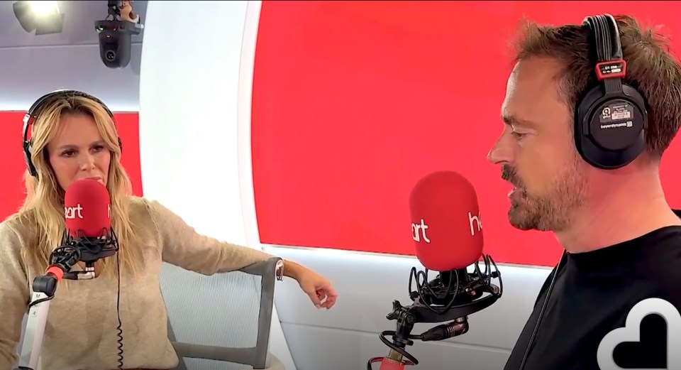 Jamie Theakston, facing right, speaks into a red Heart radio microphone while Amanda Holden, facing forward, listens.