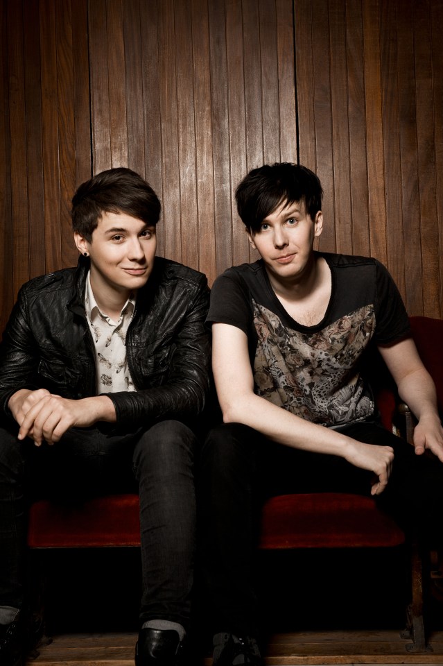 Dan Howell and Phil Lester sitting against a wooden wall.