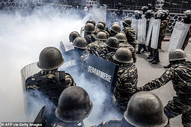 Members of the Malagasy gendarmerie take cover behind their shields amid tear gas during clashes between demonstrators and security forces in protests