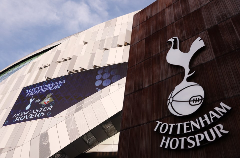 The Tottenham Hotspur Stadium exterior with a large screen displaying "Tottenham Hotspur vs Doncaster Rovers" and the Tottenham Hotspur logo.