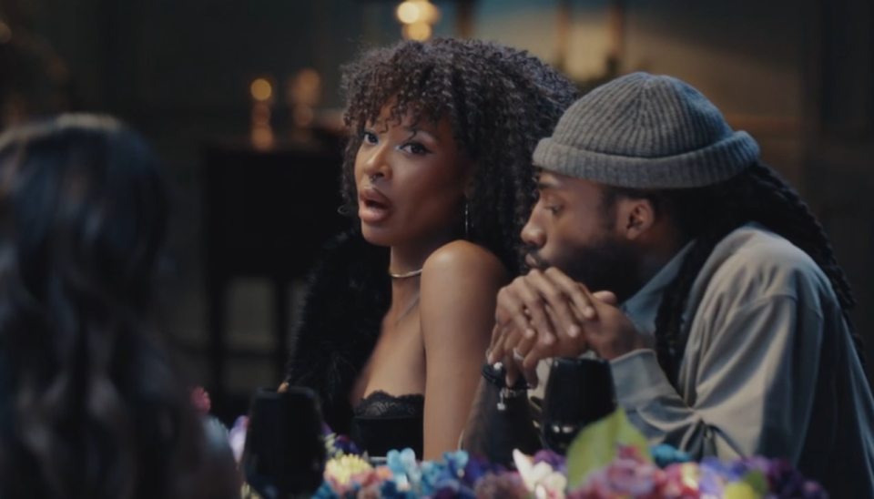 A woman with curly hair and a man in a beanie hat at a dining table.