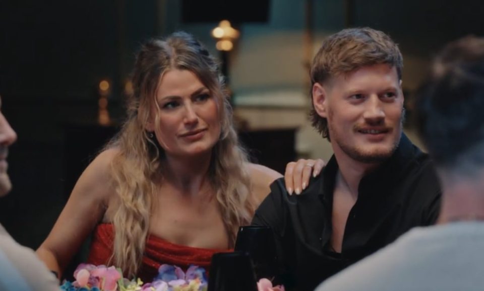 A woman in a red dress with her arm around a man in a black shirt, both smiling.