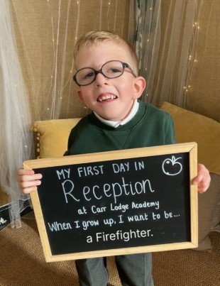 Freddie Michael Webster holding a sign that says, "My first day in Reception at Carr Lodge Academy. When I grow up, I want to be a Firefighter."
