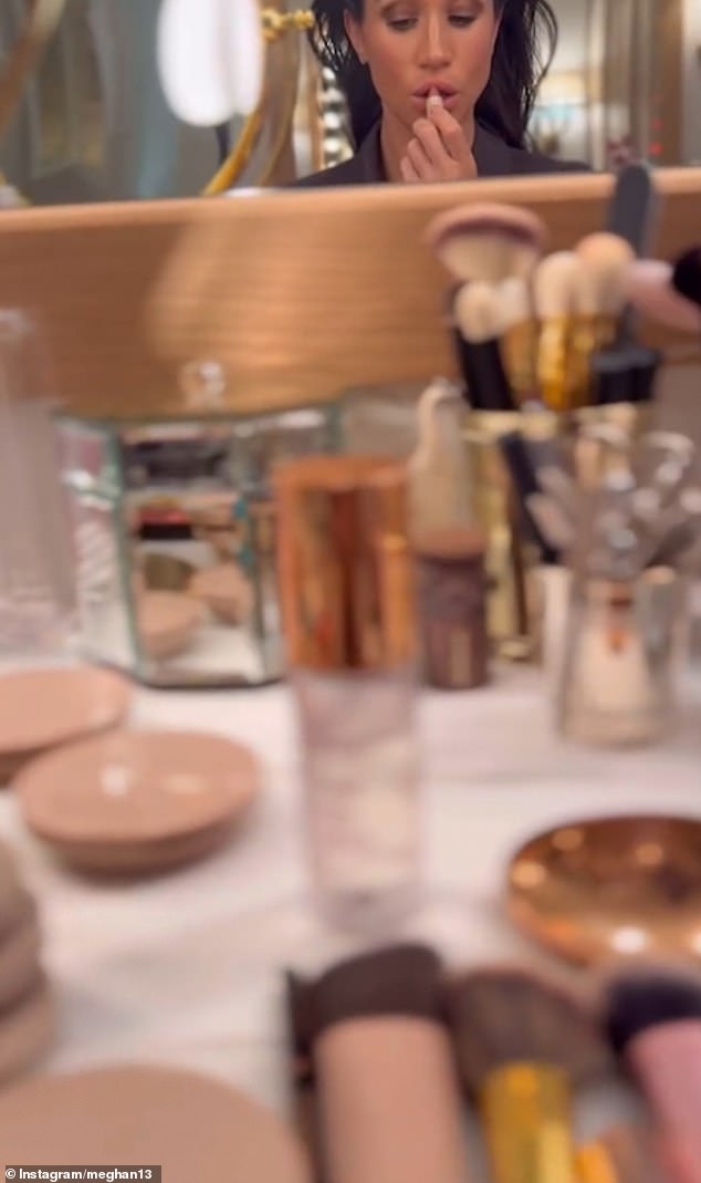 Meghan gives an insight into her makeup routine, zooming in on the array of cosmetics bottles and brushes on her dressing table as she is spotted applying bright pink lipstick in the mirror