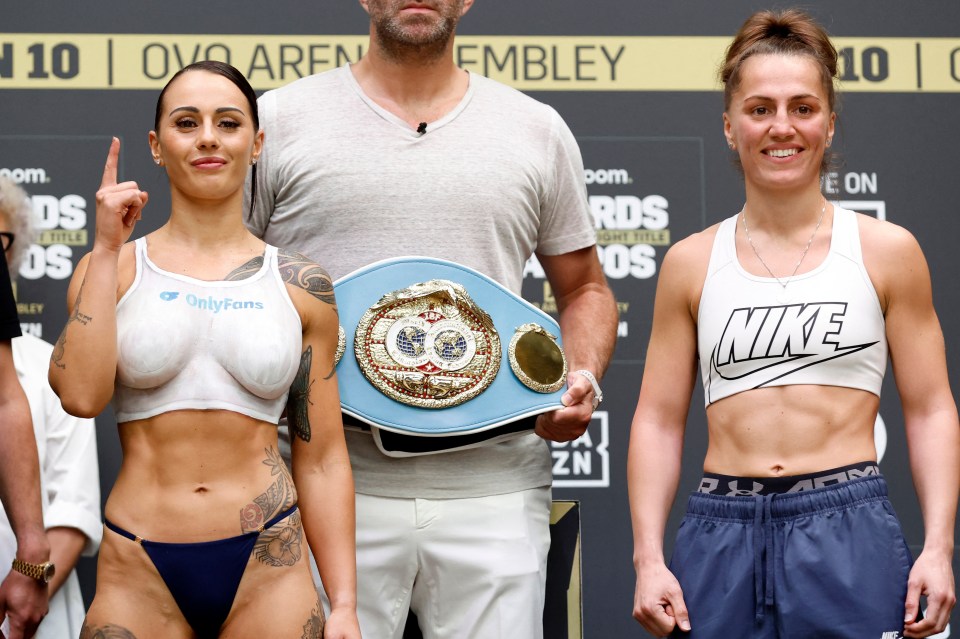 Cherneka Johnson, wearing a white sports bra painted with "OnlyFans", and Ellie Scotney, in a white Nike sports bra, during a boxing weigh-in, with promoter Eddie Hearn holding a championship belt between them.