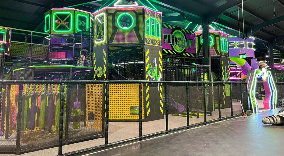 The interior of the Flip Out trampoline park, featuring multi-level structures with neon green and purple lighting.