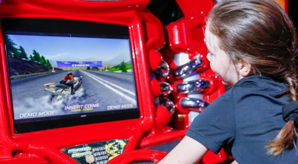 A young girl playing a motorcycle racing arcade game.