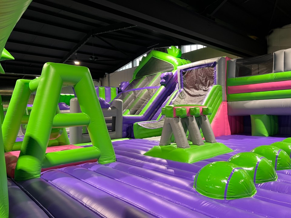 Indoor trampoline park with inflatable green, purple, and pink structures.