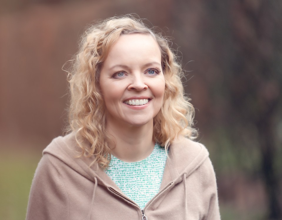 A smiling blonde woman with curly hair looks up and to the right.