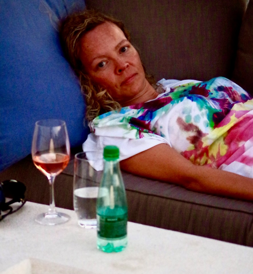 Sandra Parker resting on a couch with a glass of rosé wine and a bottle of water on a table in the foreground.