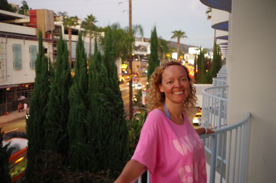 Sandra Parker smiling on a balcony overlooking a city street at dusk.