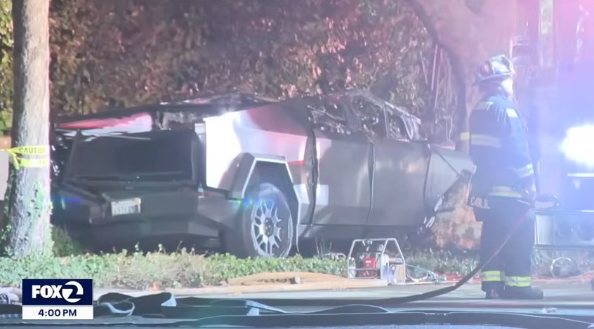 A firefighter stands next to a Tesla Cybertruck crashed into a tree.