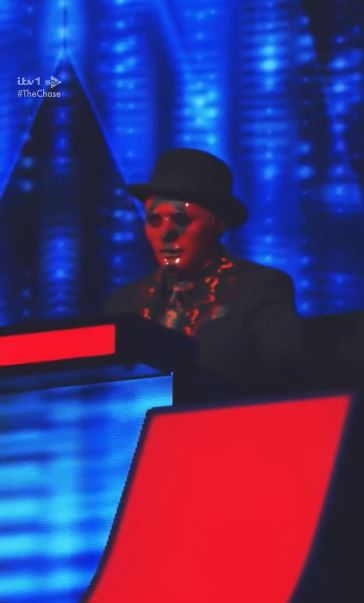 The new Beat The Chasers star, Darragh, wearing a black hat and red makeup, with a blue background.