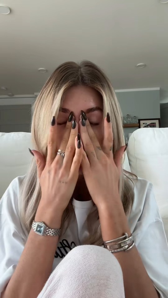 Kate Cassidy covering her face with her hands, wearing a white t-shirt and grey bottoms.