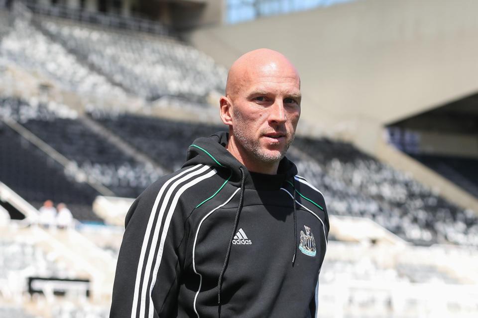 John Ruddy of Newcastle United in a black Adidas hoodie with white stripes and green trim, stands on a sunny day in St. James' Park.