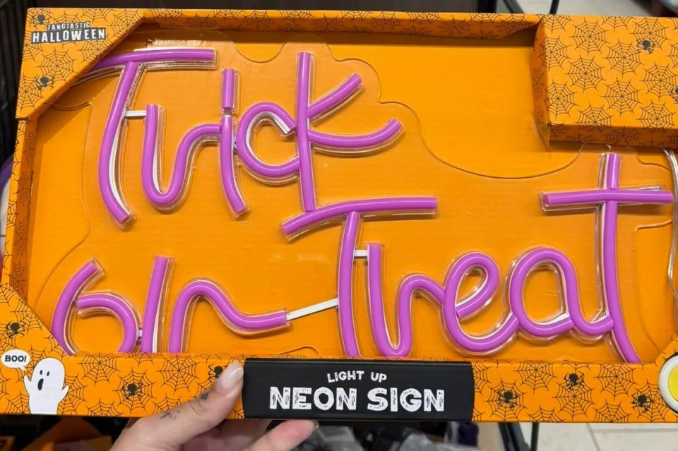 A hand holding a "Trick or Treat" neon sign in a grocery store aisle.