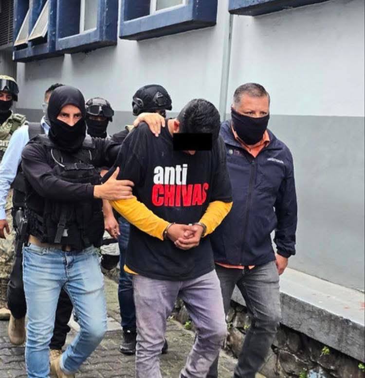 Moisés Pulido, wearing an "Anti Chivas" shirt, being escorted by police after his arrest for the murder of an opponent during an amateur football match.
