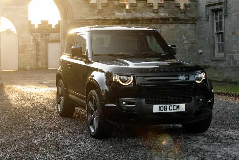 Land Rover Defender parked in front of a castle archway at sunset.