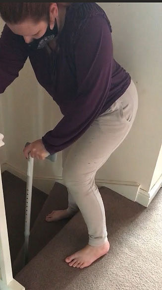 Woman using a crutch to climb stairs.