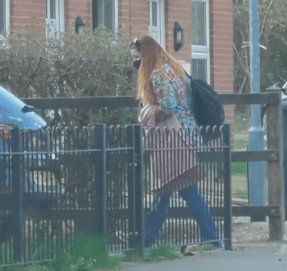 Woman wearing a face mask and carrying a backpack walks past a fence.