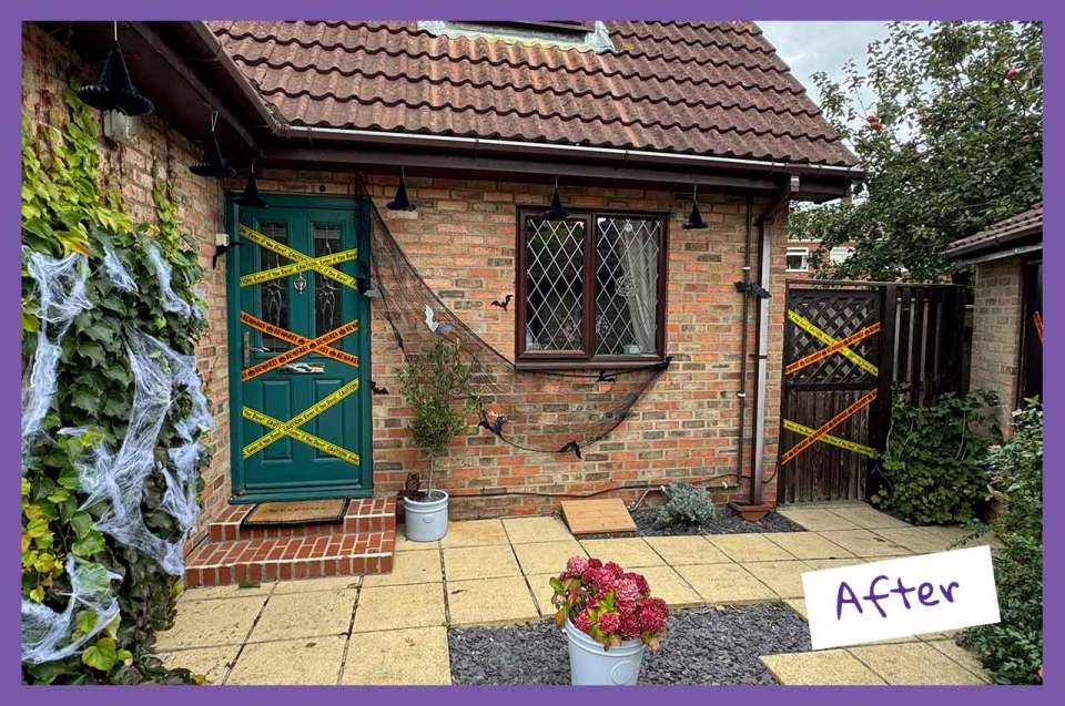 A brick house decorated for Halloween with caution tape on the door and fence, spiderwebs on ivy, and black netting with bats under the window.