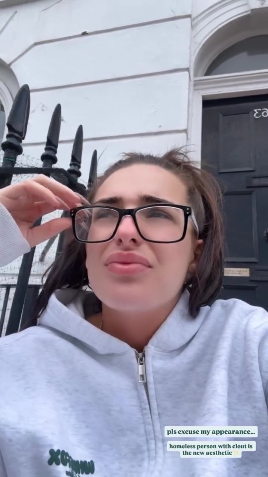 A woman with dark hair in a ponytail wearing a gray hooded sweatshirt and glasses with text "pls excuse my appearance... homeless person with clout is the new aesthetic ✨"