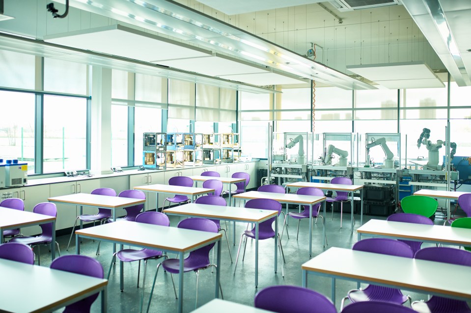 Empty classroom with purple chairs, white tables, and robotics equipment.