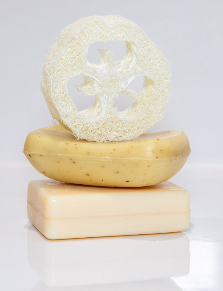 Two bars of soap and a loofah on a reflective surface.