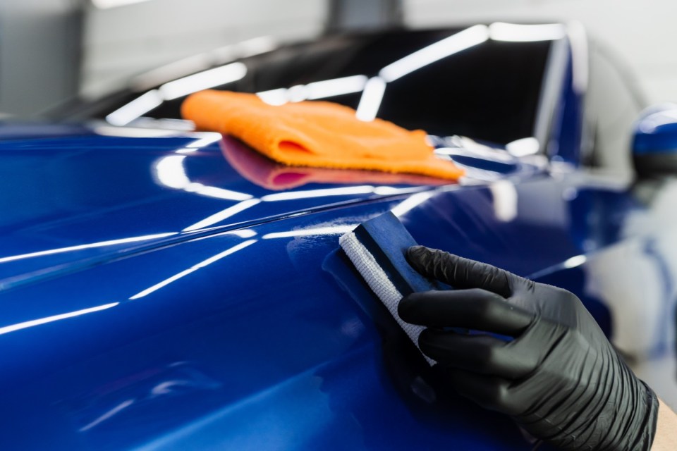 Hand in black glove applying ceramic protective coating to a blue car body using a sponge.
