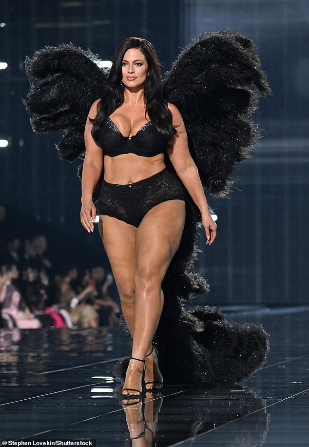 Ashley Graham put her famous curves on display in a busty black bra and semi-sheer black lace panties. She looked ready to take flight with fuzzy black featured wings and a modest train trailing behind her