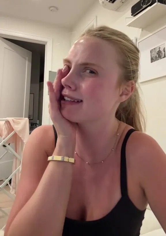 A person wearing a black top with their hand to their cheek.