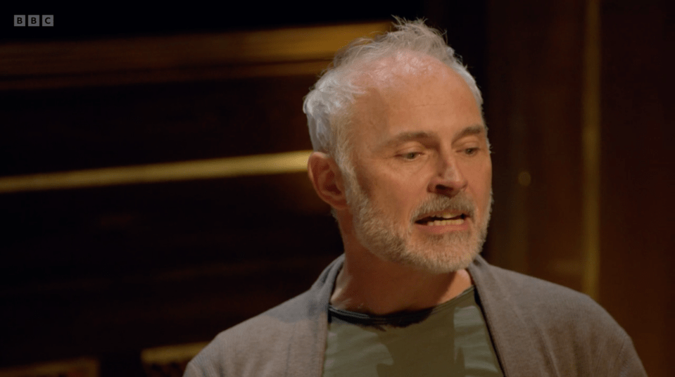 A white-haired man with a beard and a gray cardigan speaking.