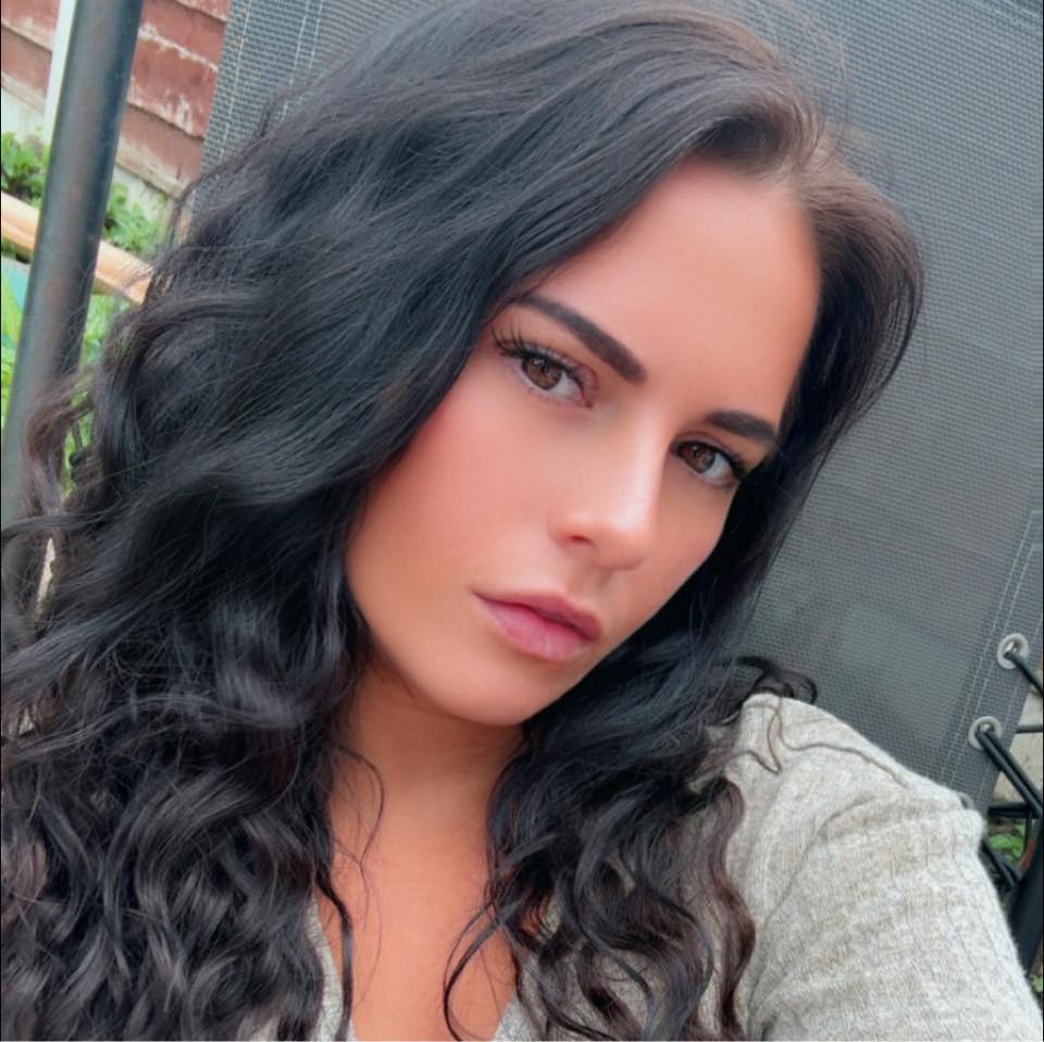 Woman with dark wavy hair and light brown eyes looking at the camera.